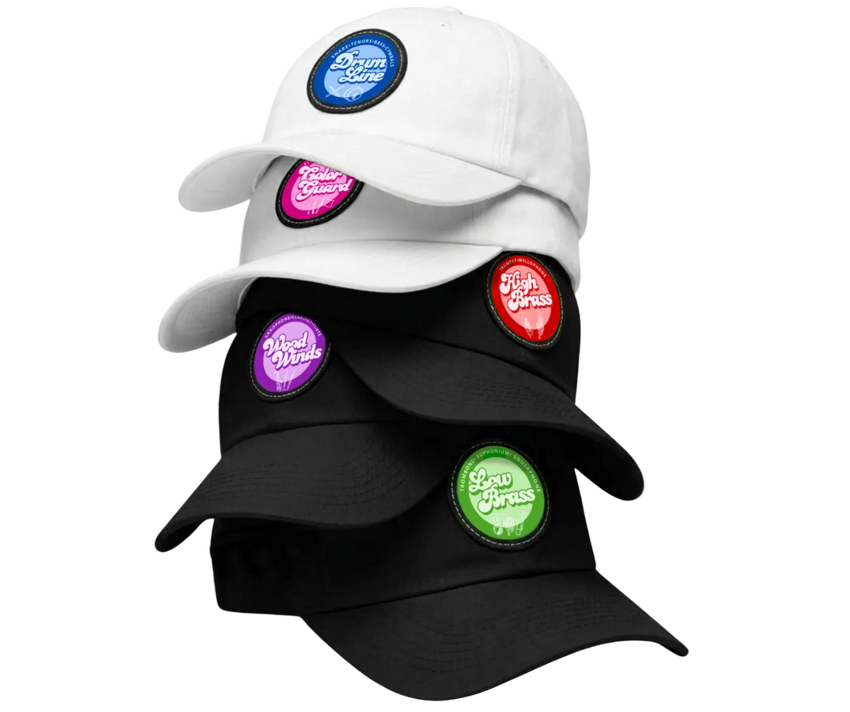 Three baseball caps stacked together on a pale green background: a white cap on top, a black cap in the middle, and a black cap on the bottom. Each cap has a round embroidered patch on the front with a different color border and logo text.